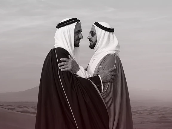 شيخان بالزي التقليدي يتعانقان في الصحراء، بالأبيض والأسود
