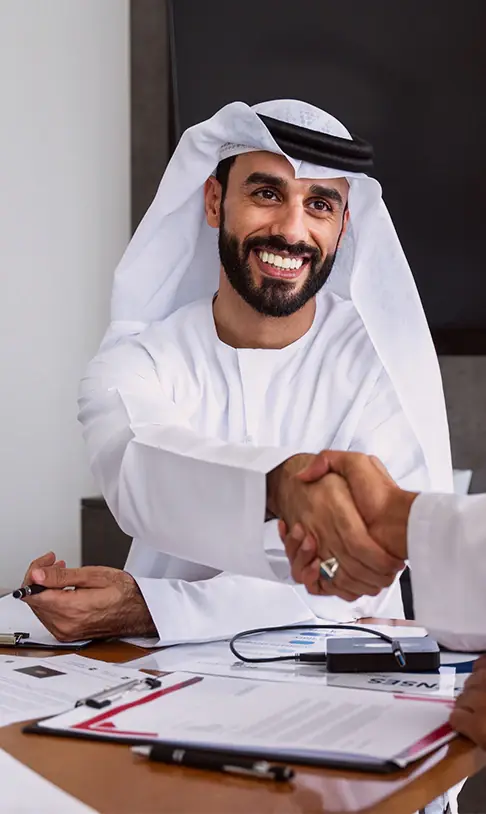 رجل مبتسم بالزي الوطني الأبيض يصافح رجلا آخر من فوق مكتب